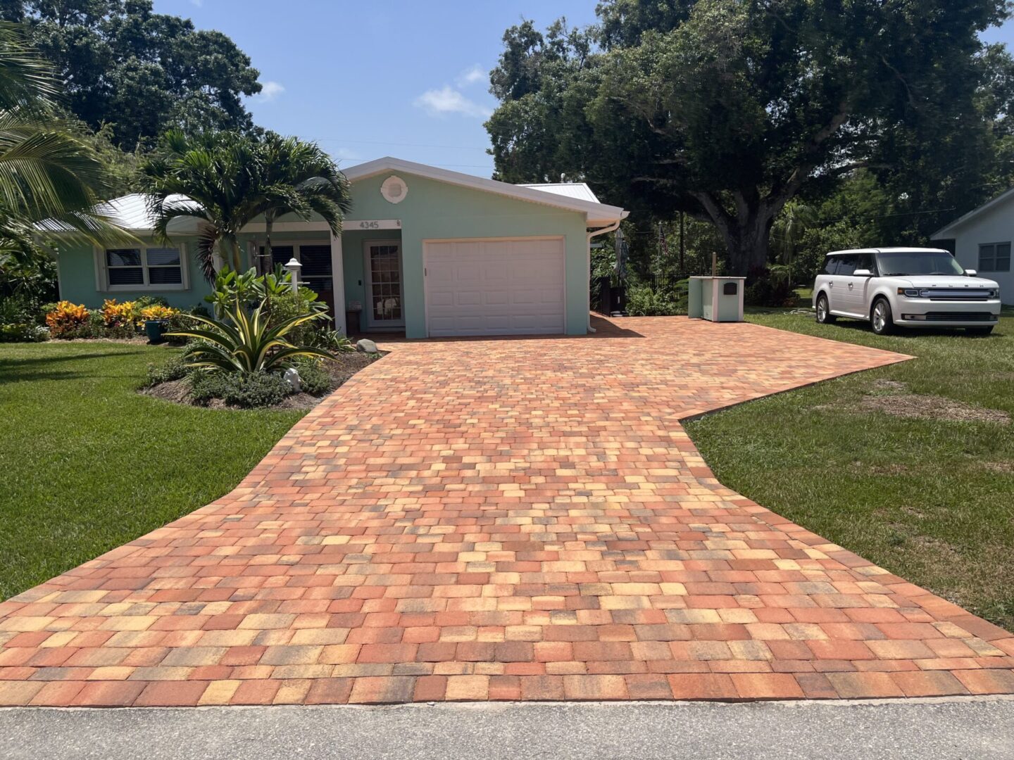 A driveway with brick pavers and palm trees in the background.