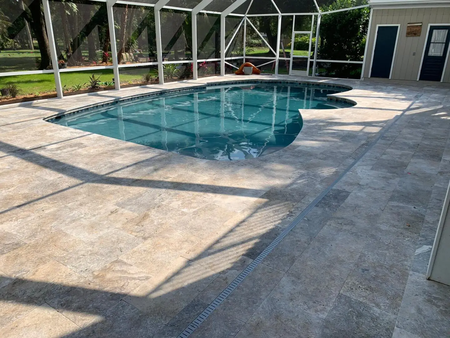 A backyard swimming pool with a stone patio and a screened enclosure. There is a storage shed adjacent to the pool.