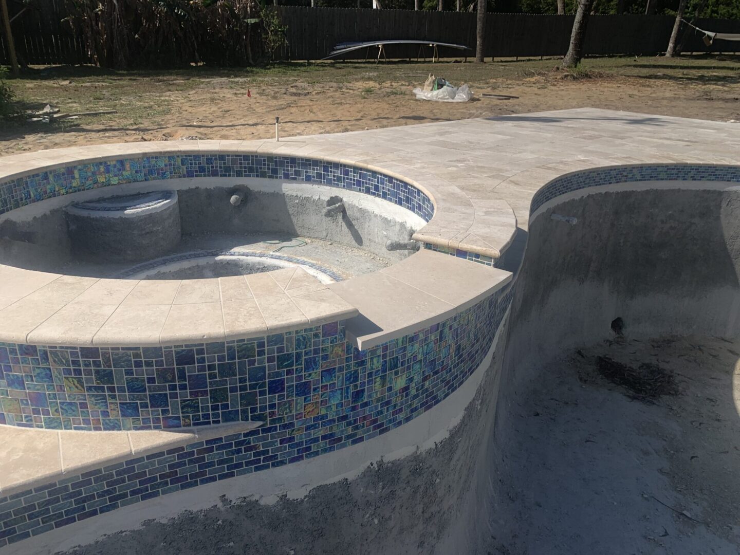 Unfinished swimming pool and hot tub with exposed concrete and a partially tiled surface in a backyard setting.