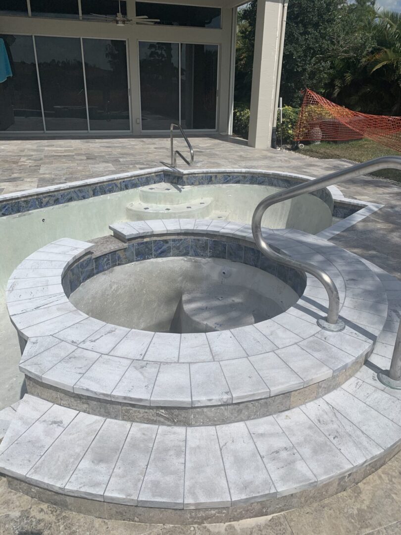 An empty in-ground hot tub with steps leading down into it, adjacent to a partially filled pool, in a backyard under construction.