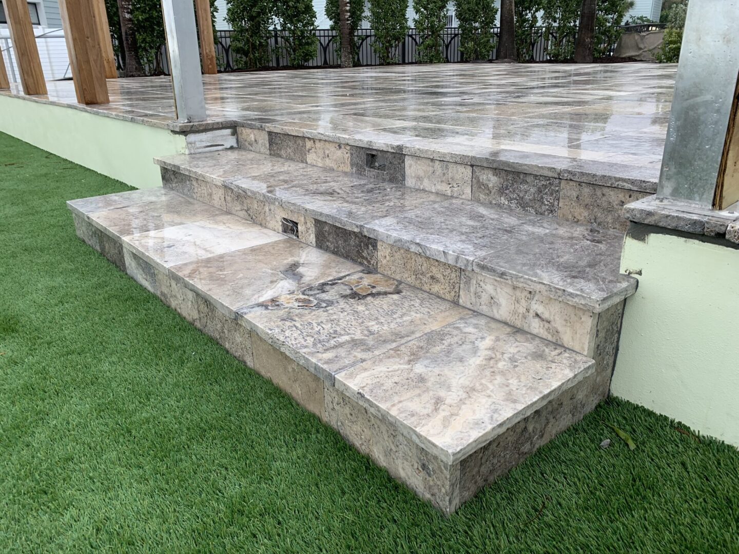 A set of three marble steps leading up to a stone patio, surrounded by manicured synthetic grass in an outdoor area.