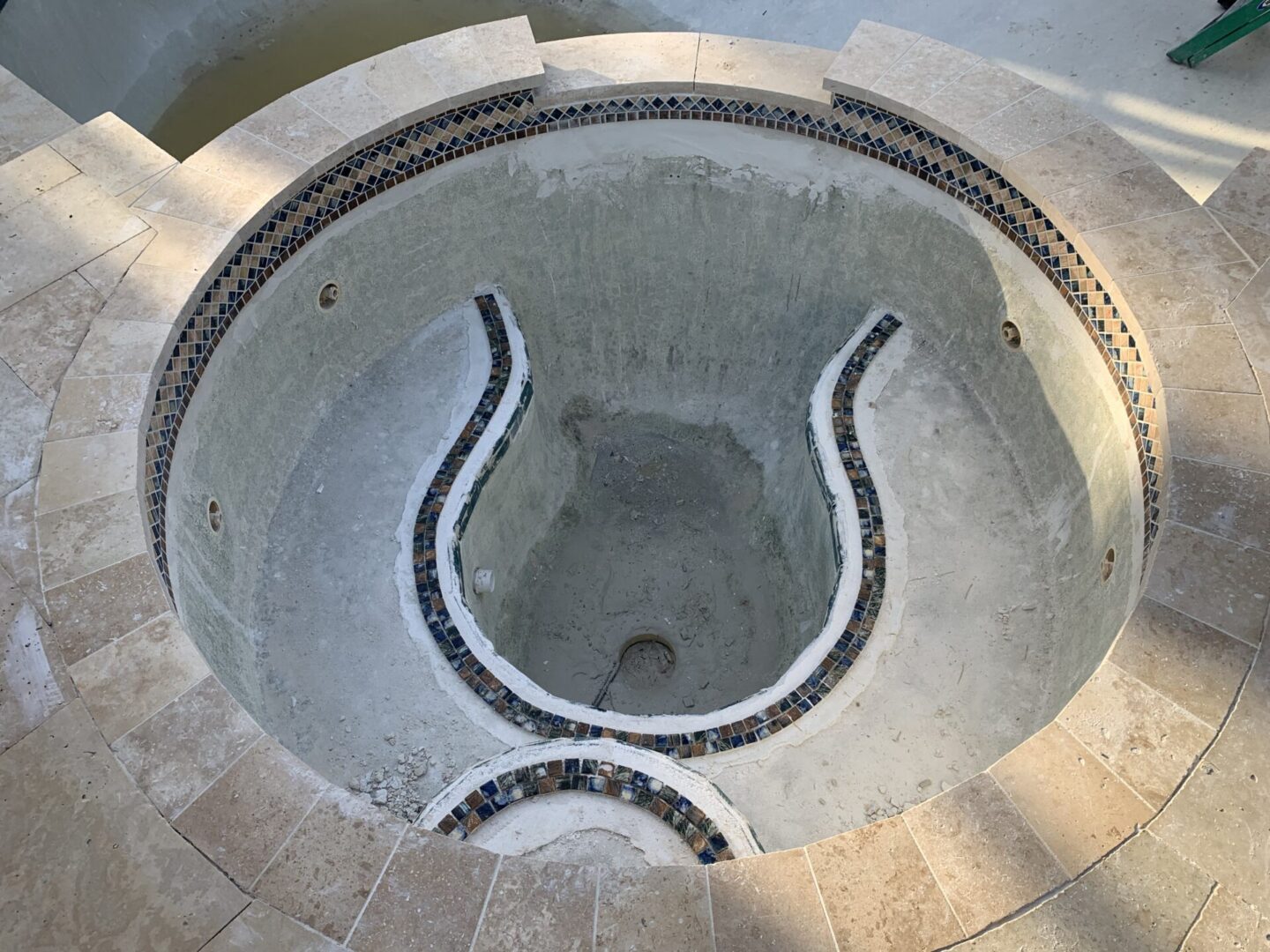 A drained circular spa under construction, featuring tiled edges and a curved, stepped interior design.