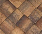 A close-up view of a textured pattern of overlapping, brown shingles on a roof.